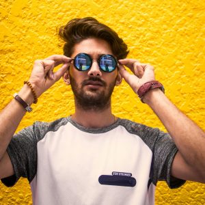 Man in White and Gray Shirt Wearing Sunglasses Against Yellow Wall